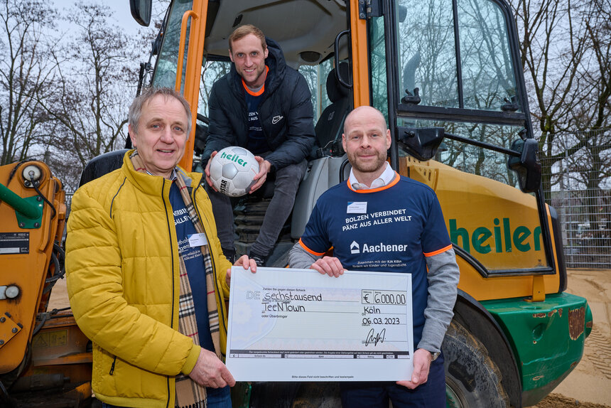 Zwei Männer zeigen einen Spendenschein mit einer 6000€ Beteiligung der Aachener SWG an der Spendenaktion für einen Bolzplatz